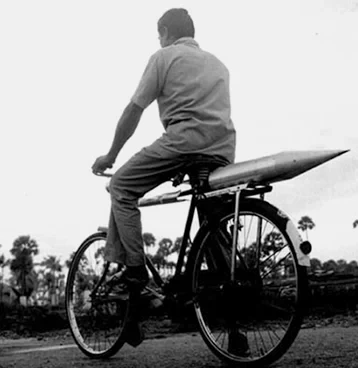 Two ISRO scientists walking alongside a bicycle carrying a large rocket component during India's early space missions.